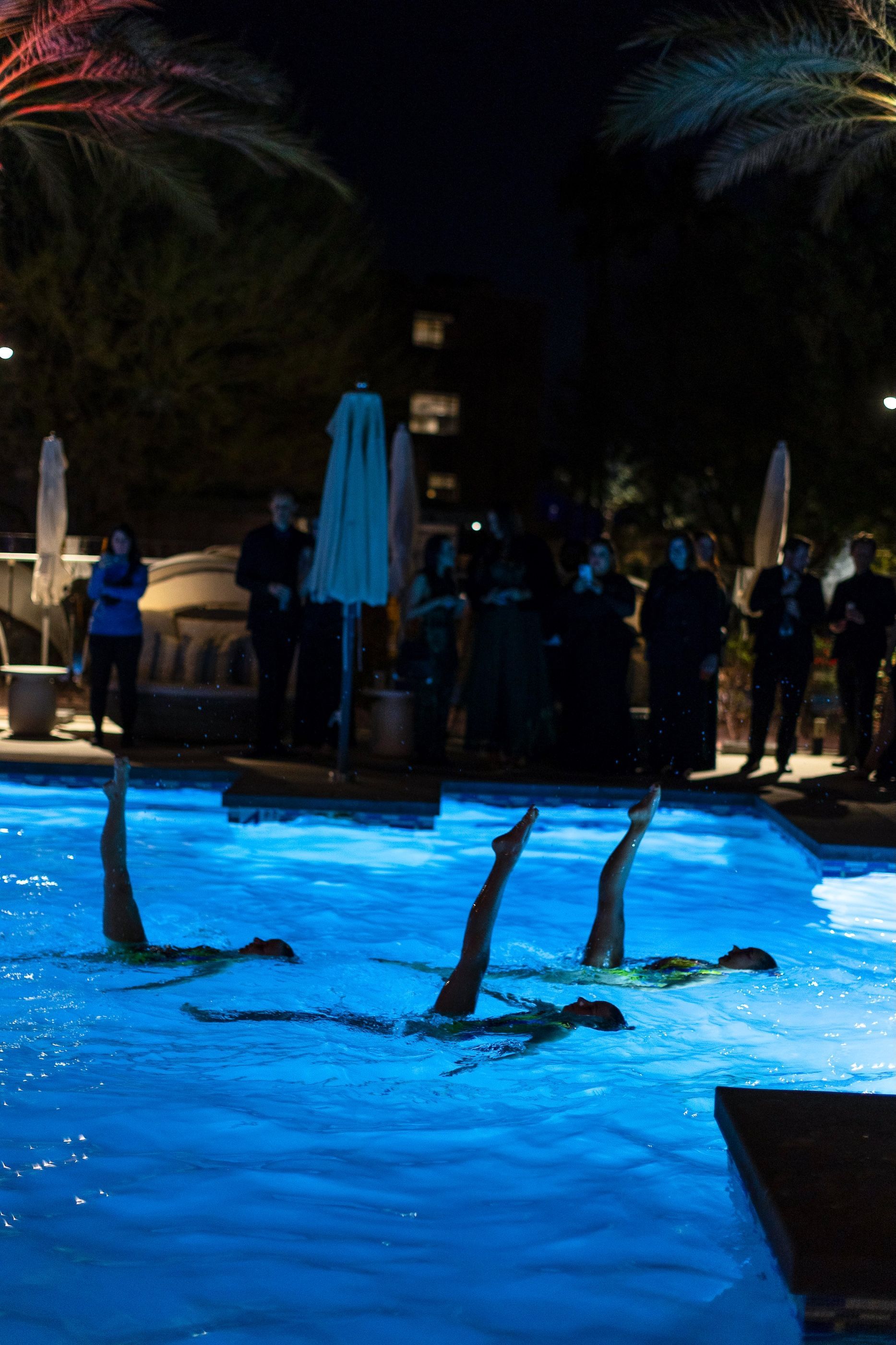 A group of people are swimming in a pool at night