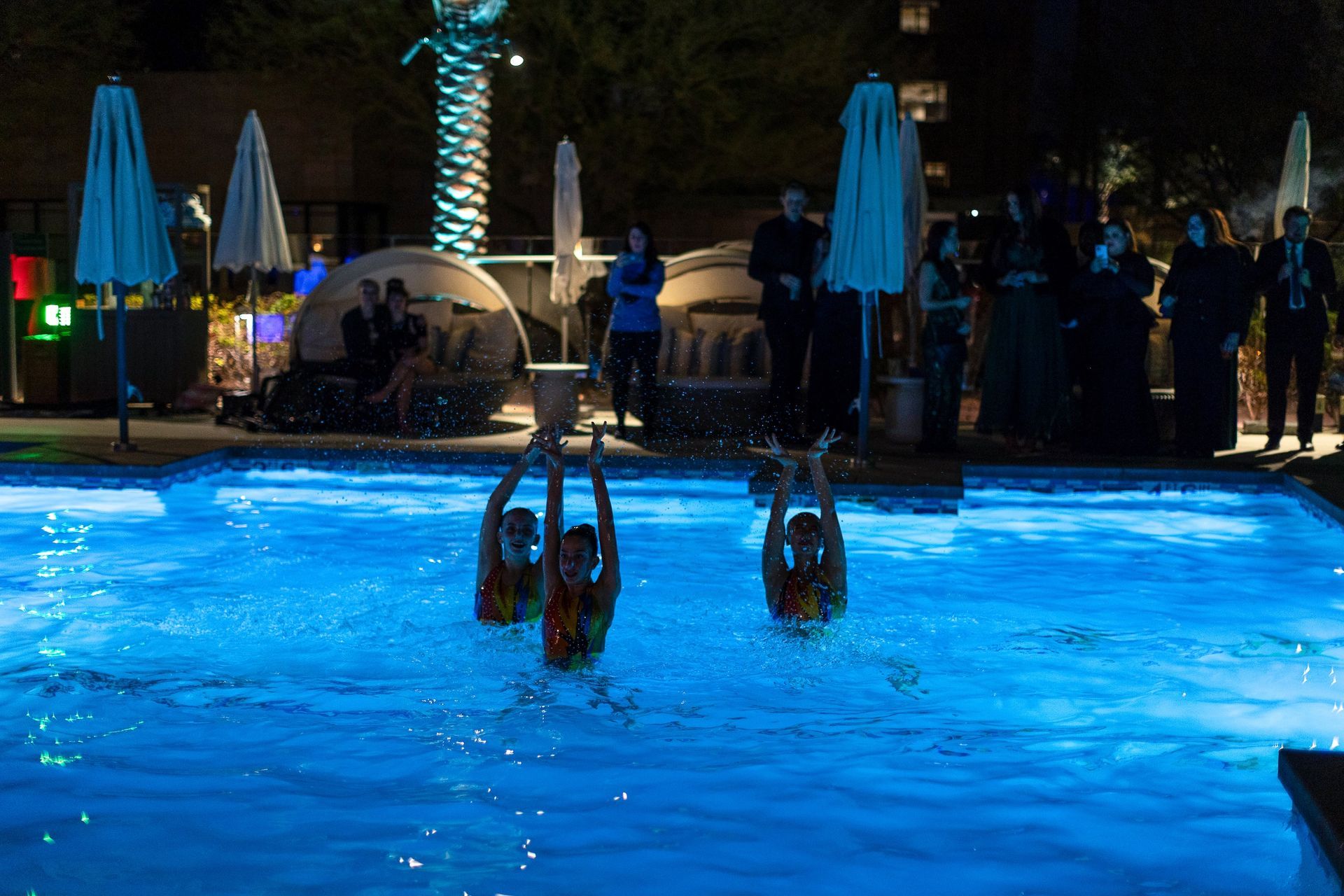 A group of people are standing around a swimming pool at night.