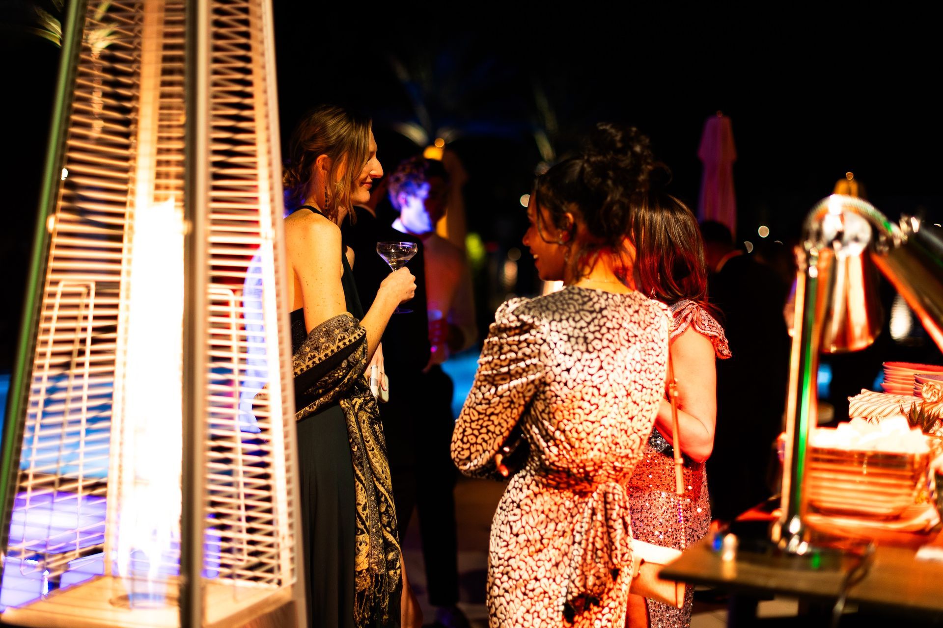 A group of women are standing around a heater at a party.