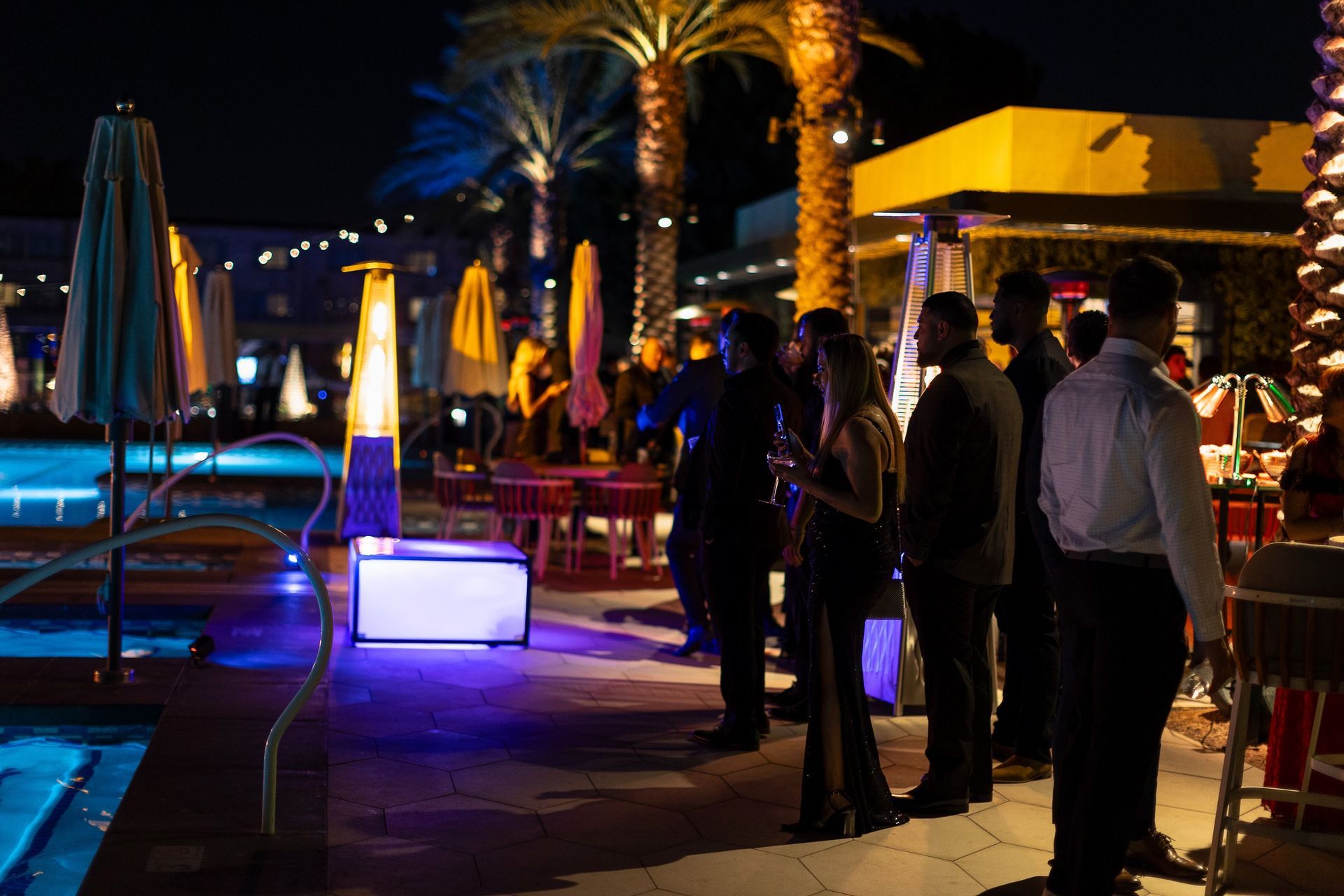 A group of people are standing around a pool at night.