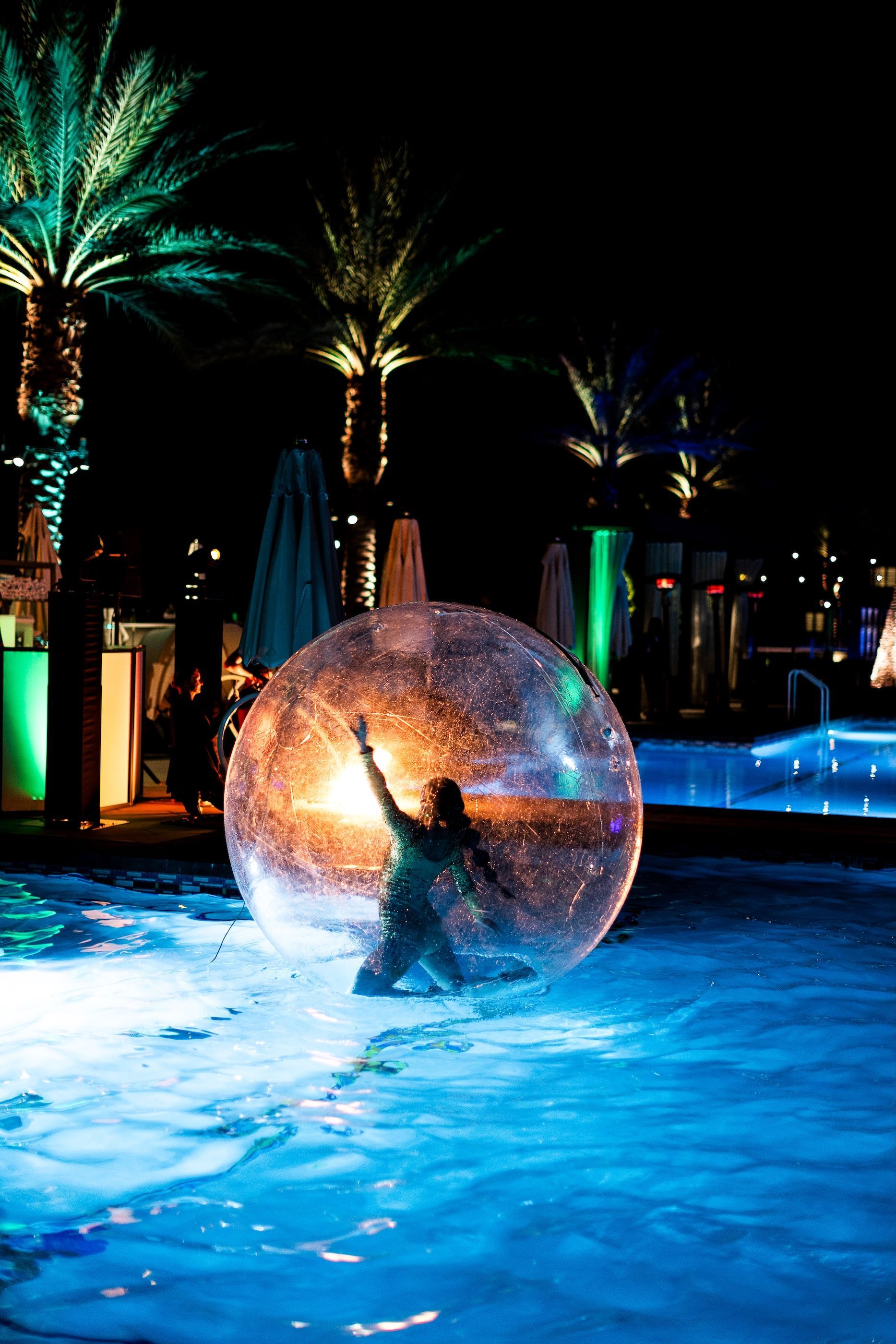 A woman is playing with a water ball in a swimming pool at night.