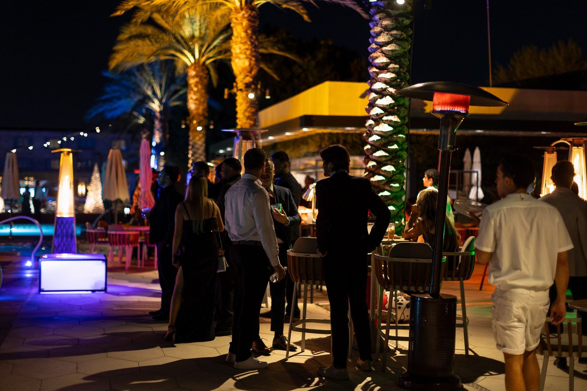 A group of people are standing around a bar at night.