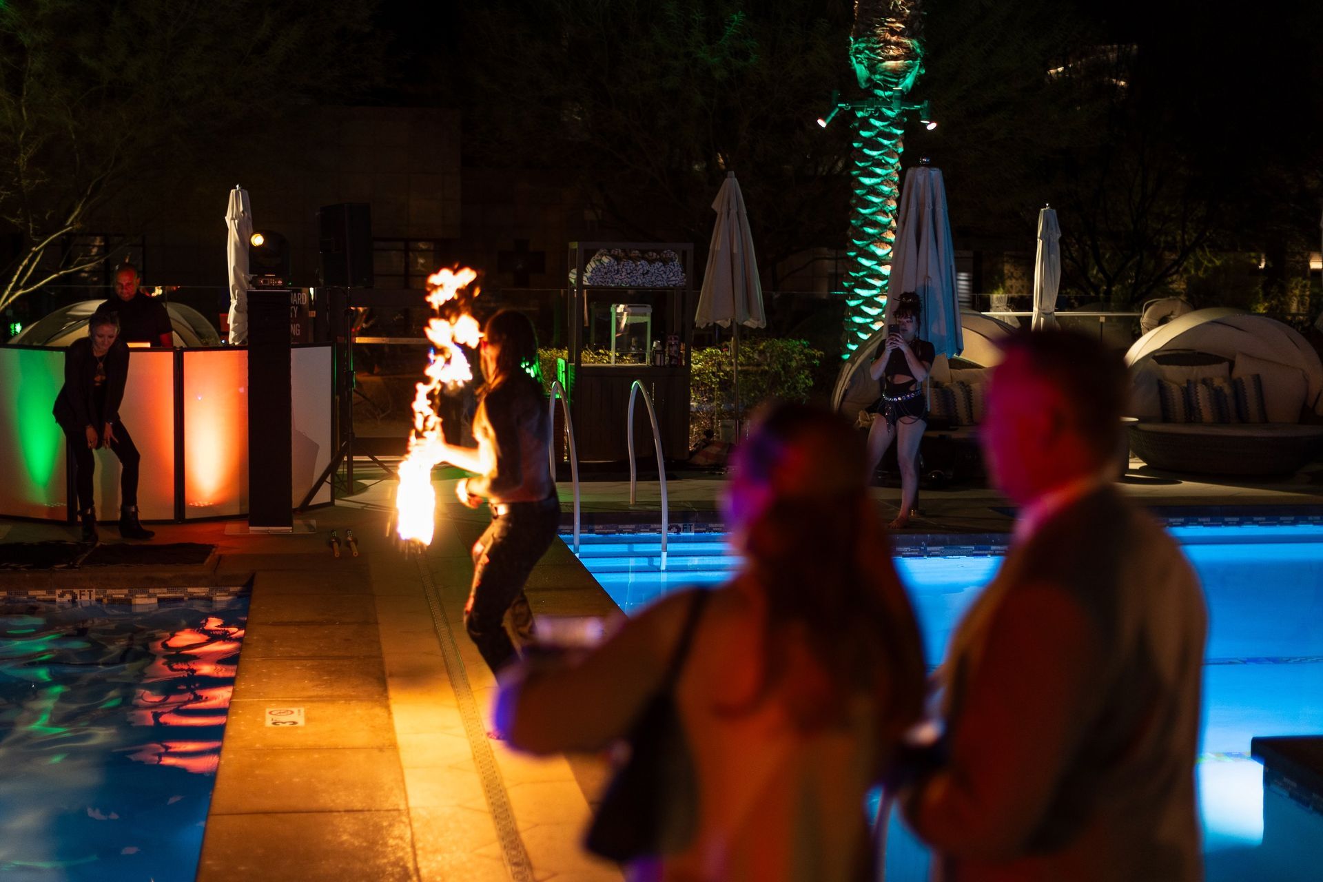 A group of people are standing around a swimming pool at night.