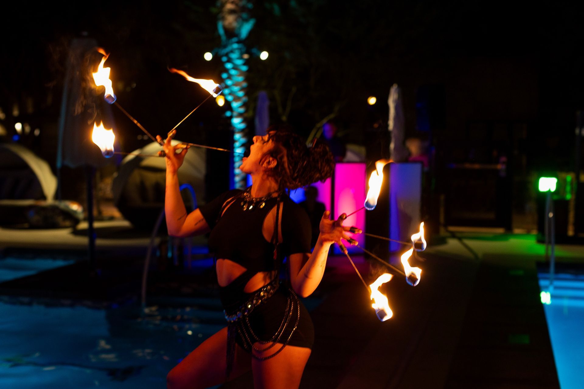 A woman is juggling fire in front of a pool at night.