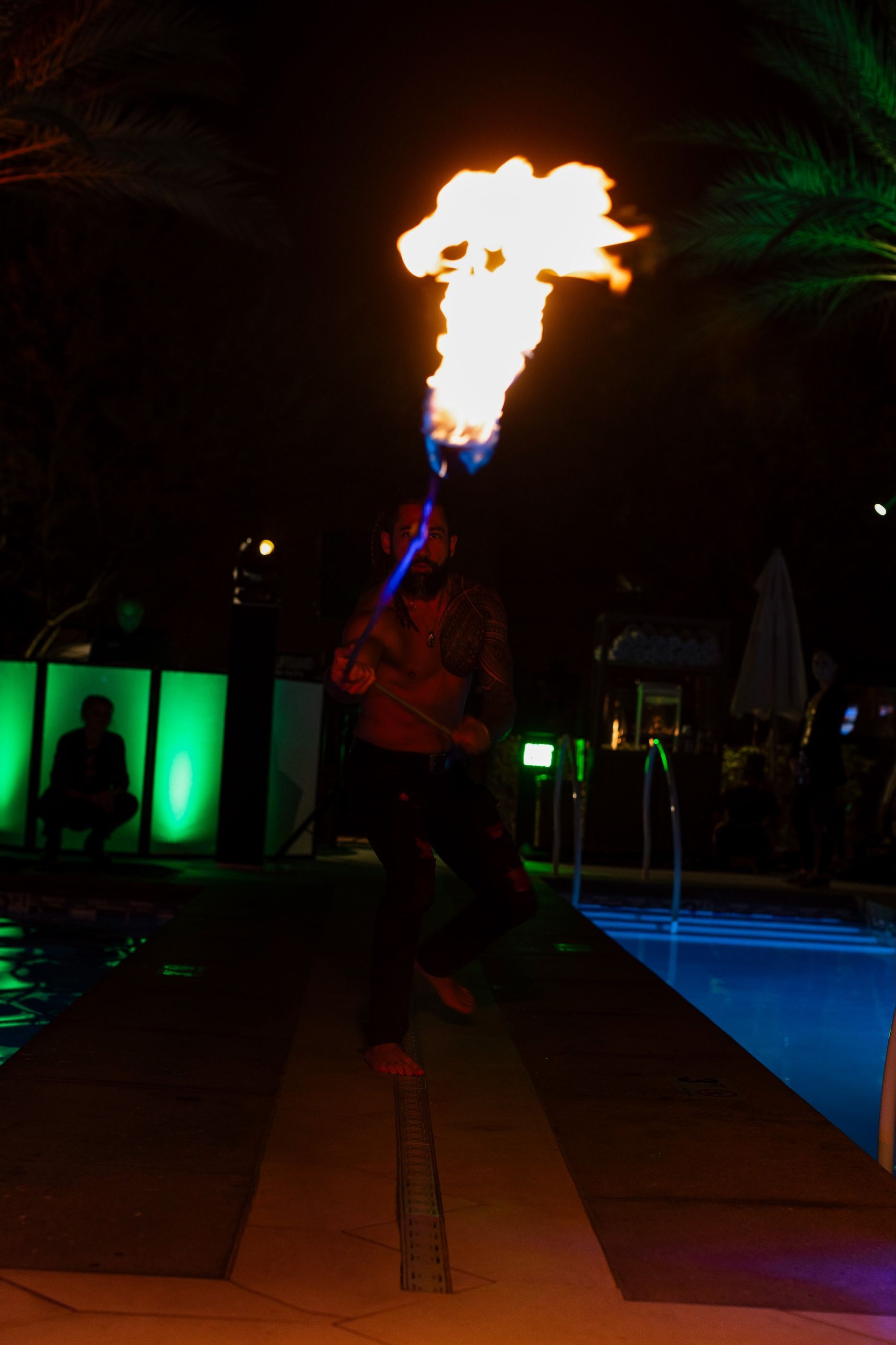 A man is holding a fire torch in front of a pool at night.