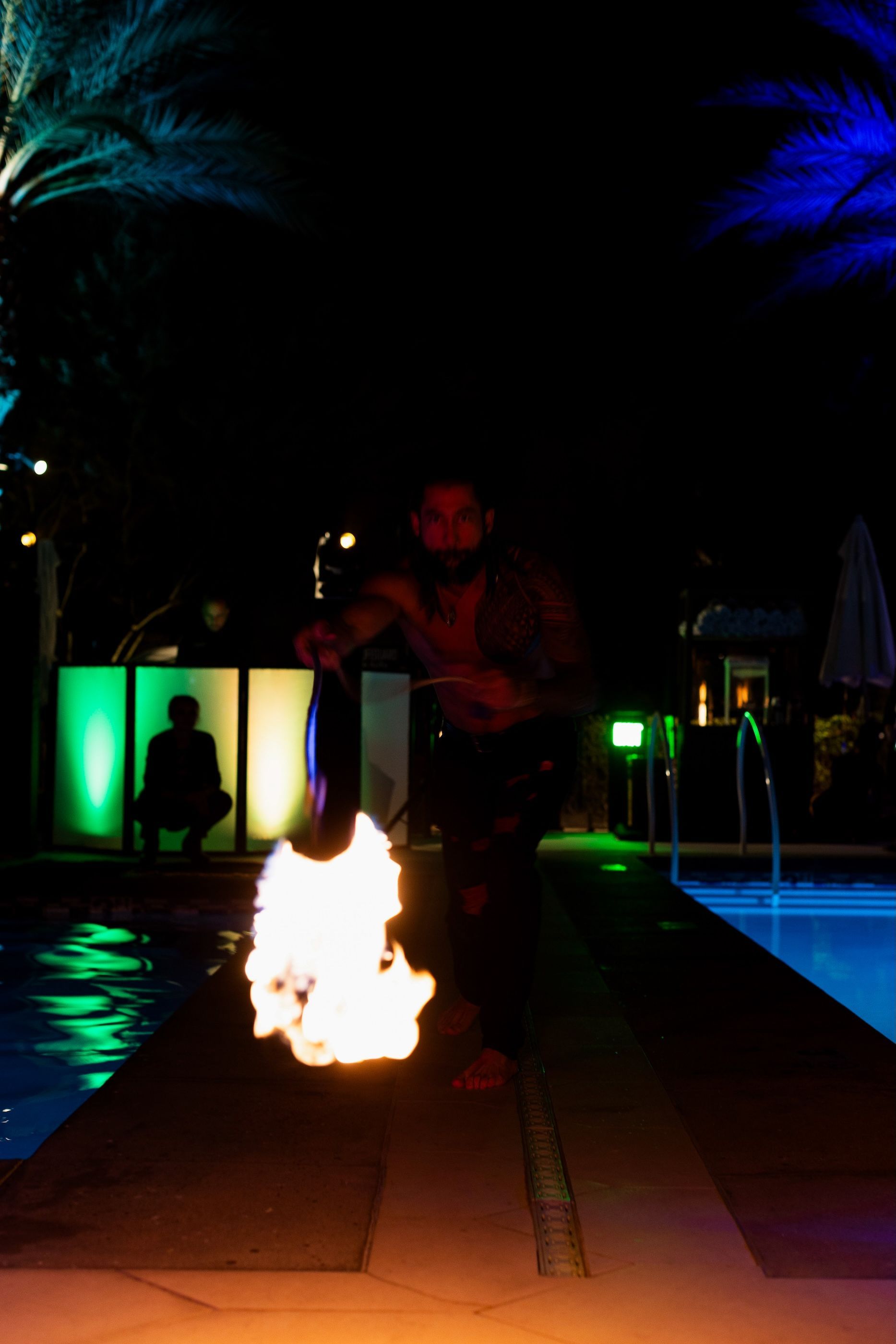 A man is standing next to a swimming pool holding a fire torch