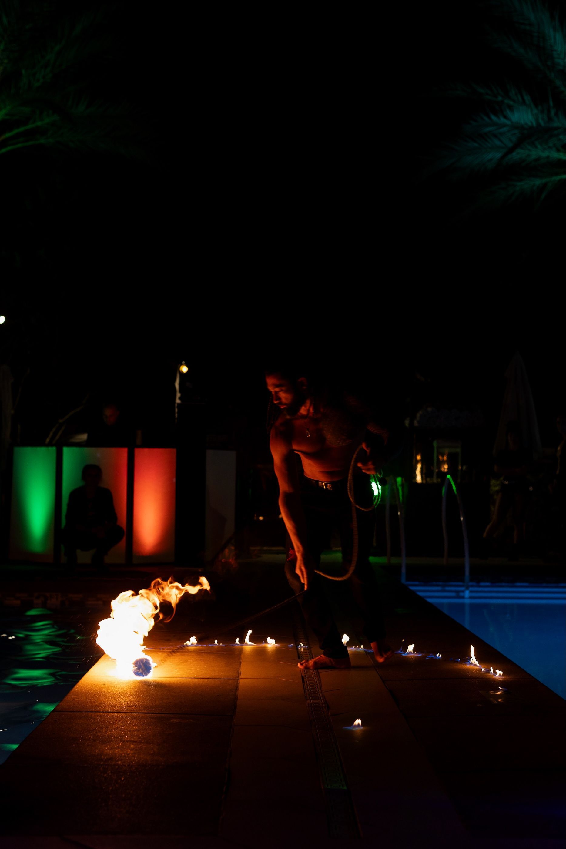 A man is standing next to a swimming pool at night holding a fireball.