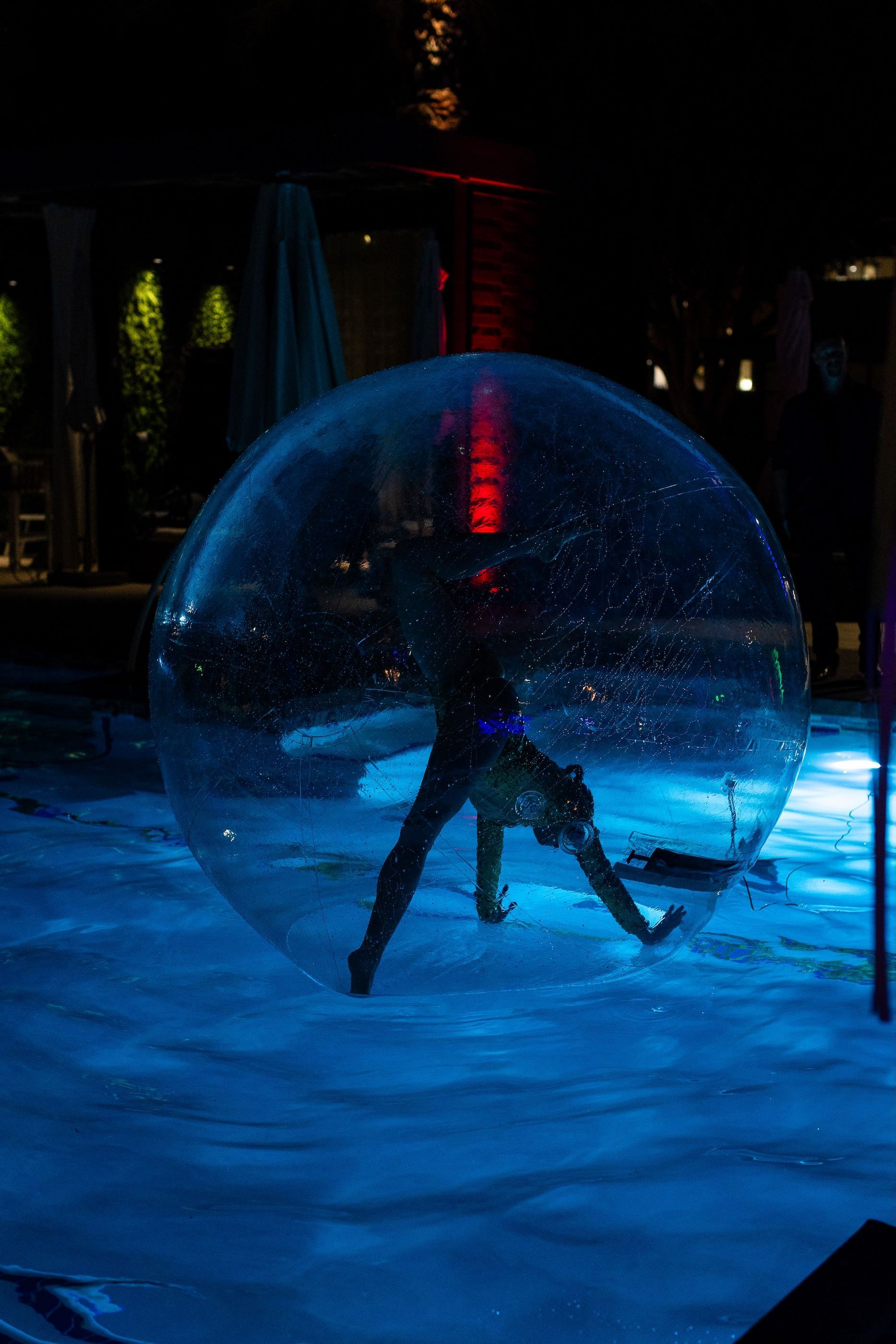 A person is standing inside of a bubble in a pool at night.