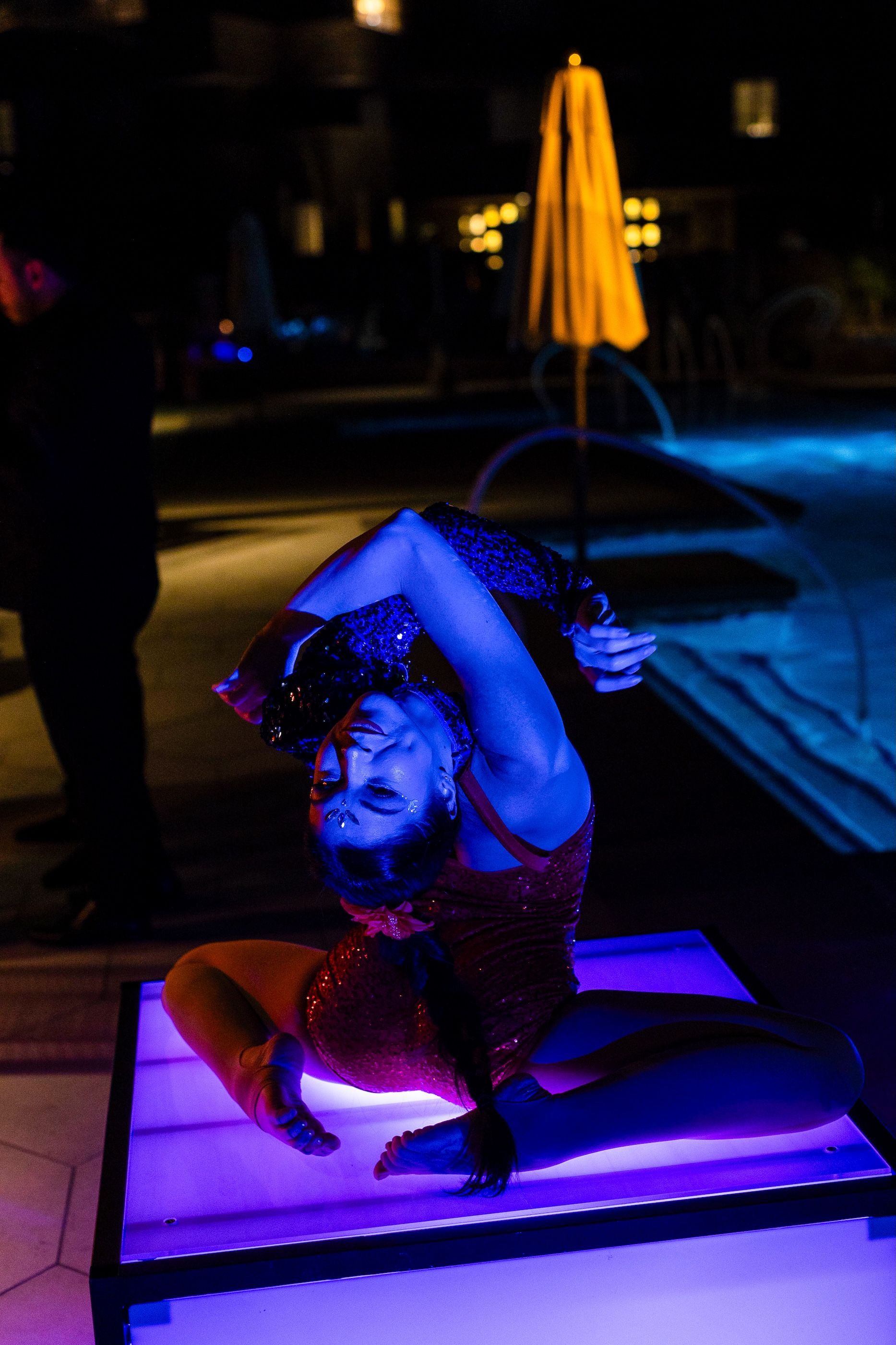 A woman is doing a handstand on a table in front of a pool at night.