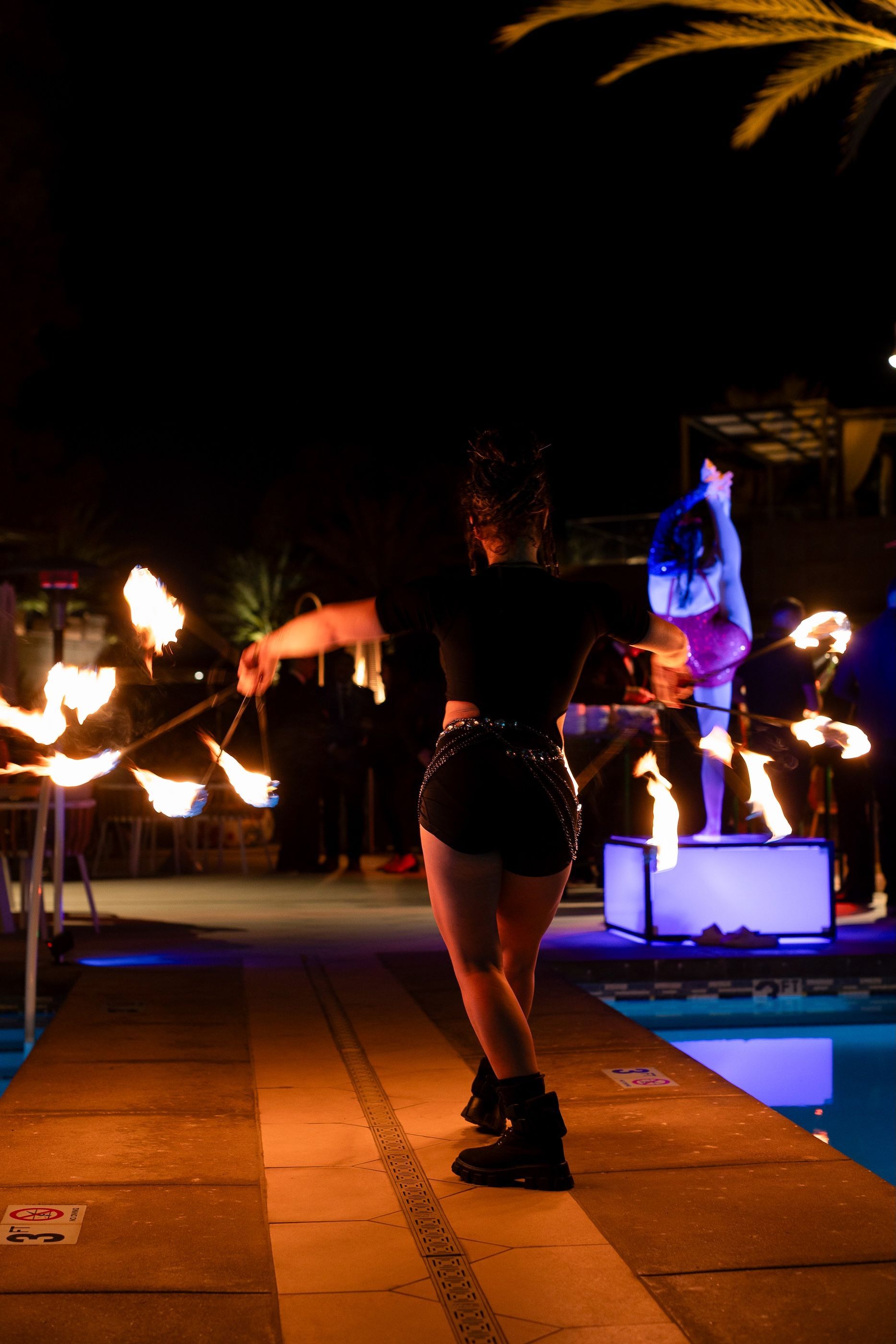 A woman is standing next to a pool holding Fire Fans.
