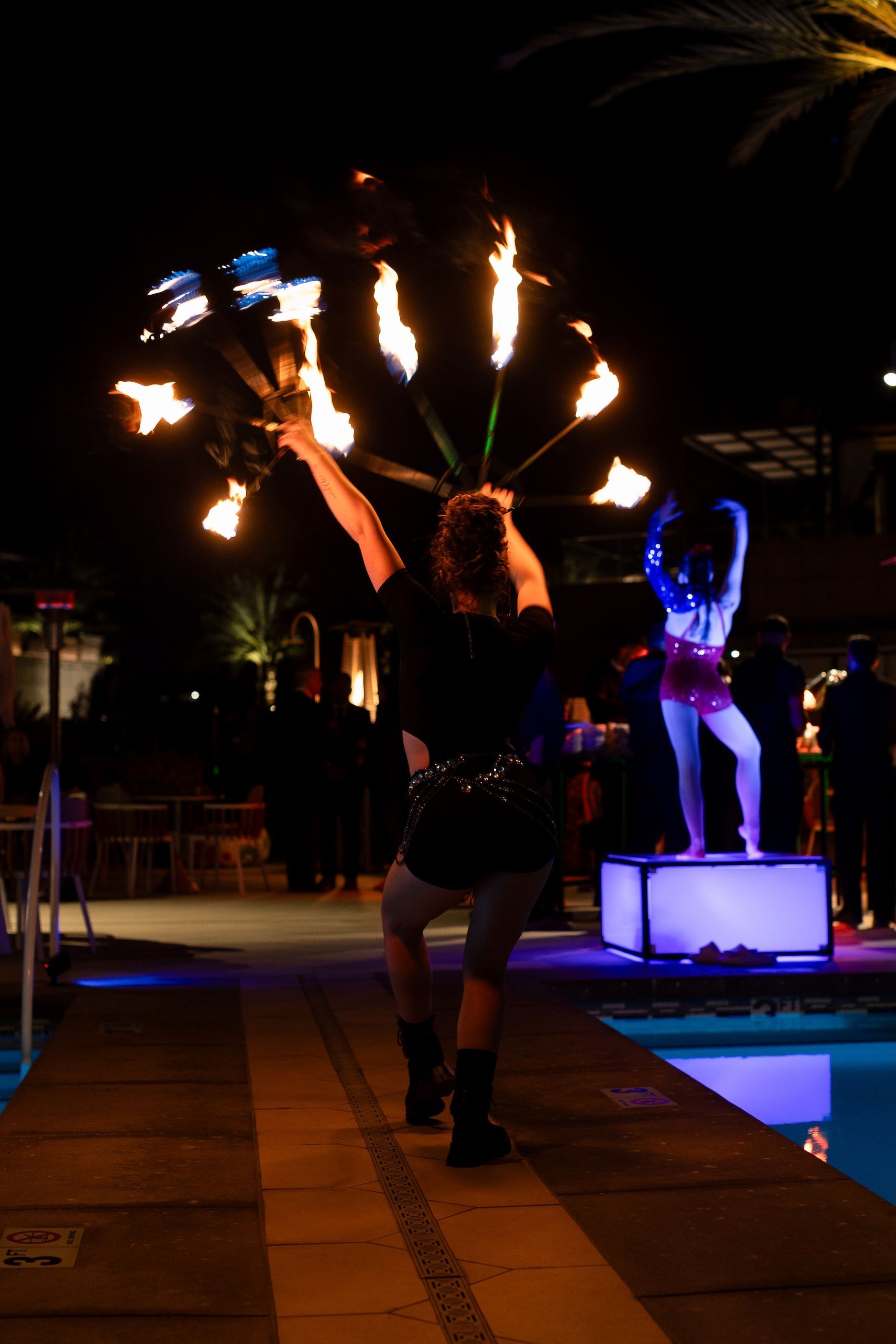 A woman is holding a fan of fire in front of a pool at night.