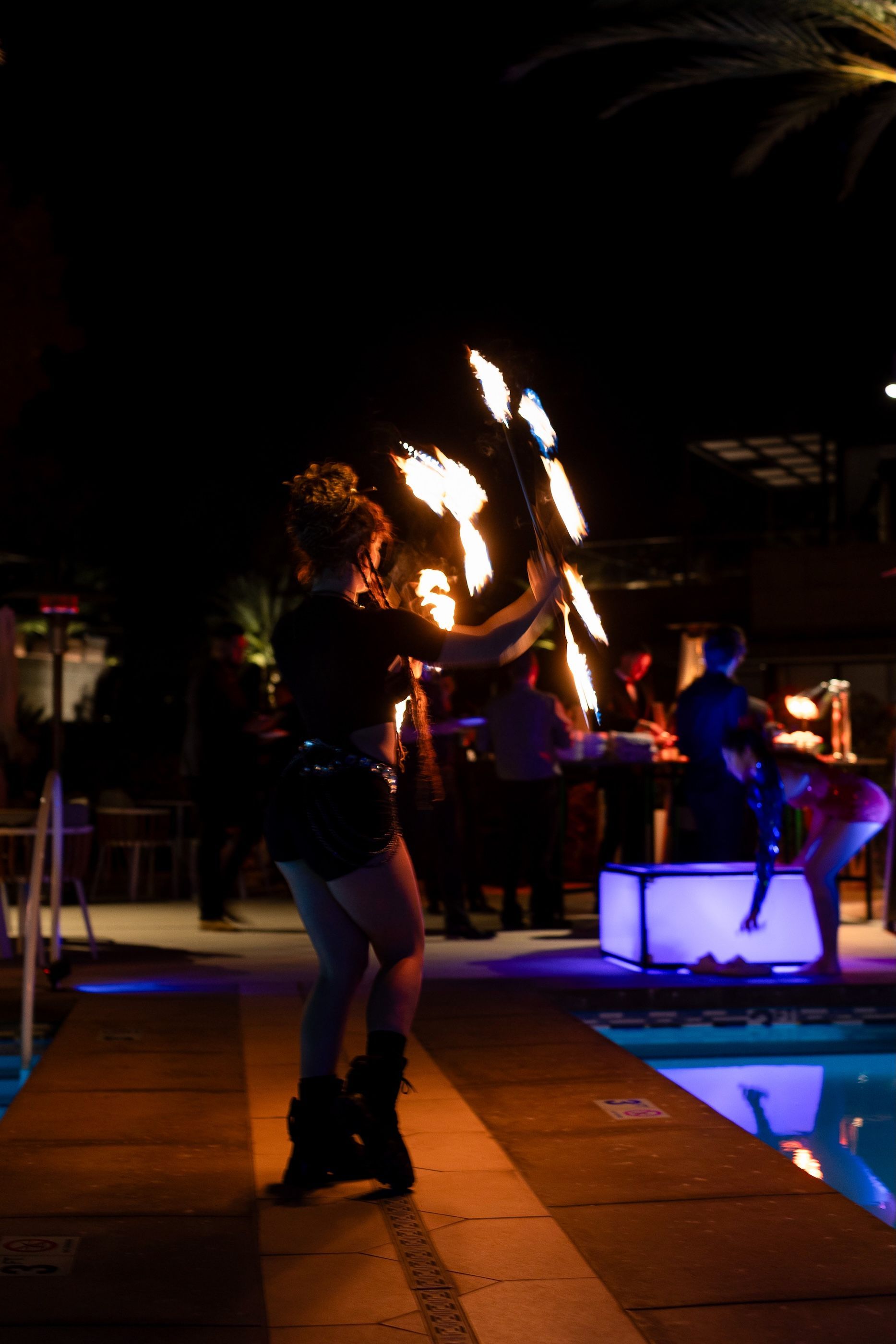 A woman is holding a torch in front of a pool at night.