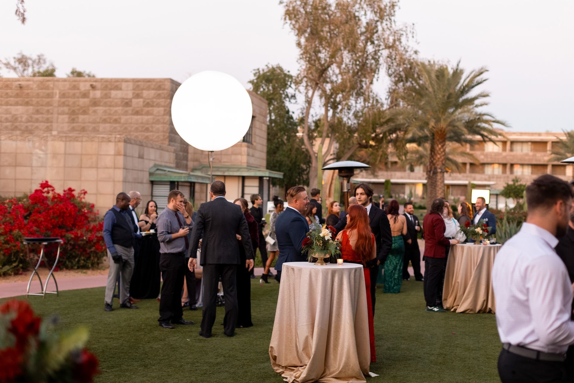 A group of people are standing around tables in a grassy area.
