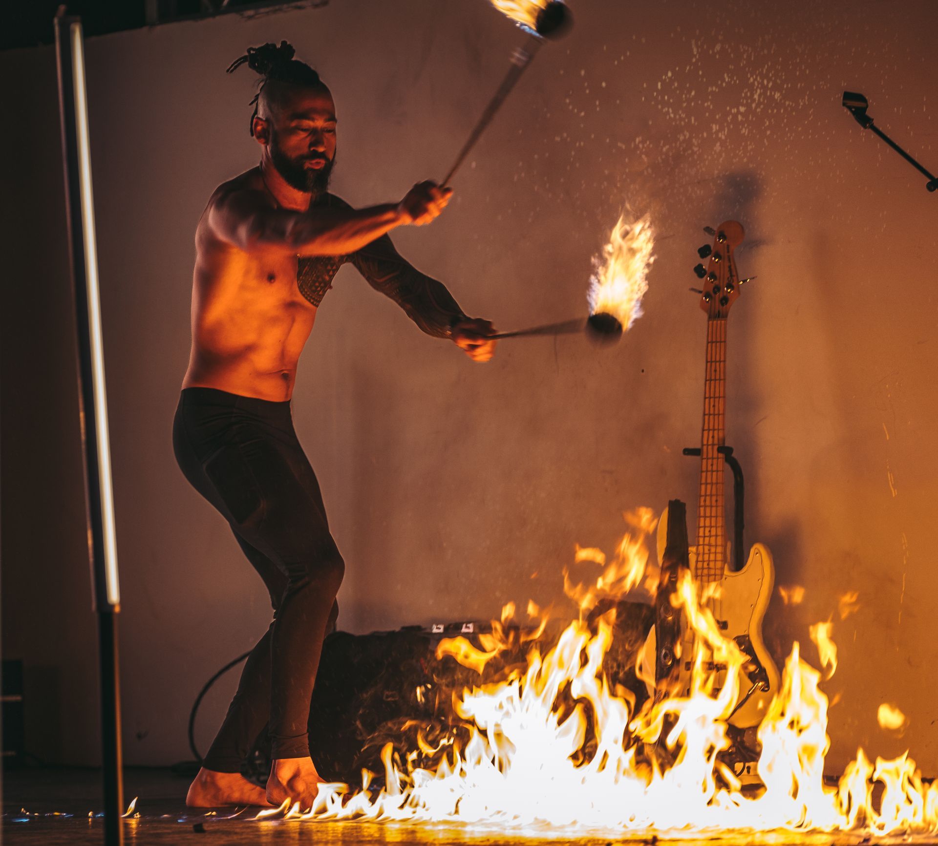 A man is juggling fire sticks in front of a guitar.