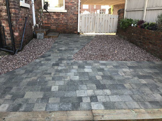A completed patio in Handforth, Wilmslow, Cheshire. Patio in Tobermore Slate Tegula block paving, sleeper steps with Tegula paving inlays, sleeper retaining wall and pink Staffordshire gravel