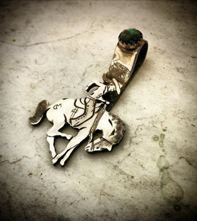 A silver pendant with a cowboy on a bucking horse