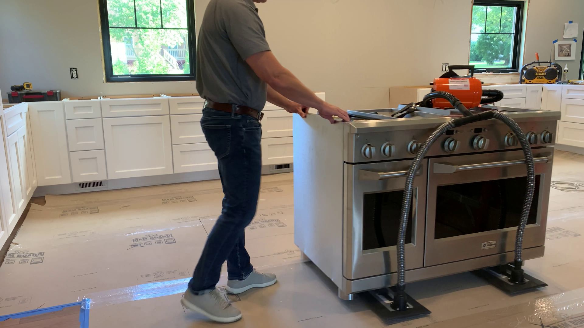 En person på et kjøkken under bygging bruker en Airsled luftslede til å flytte en stor komfyr i rustfritt stål på plass.