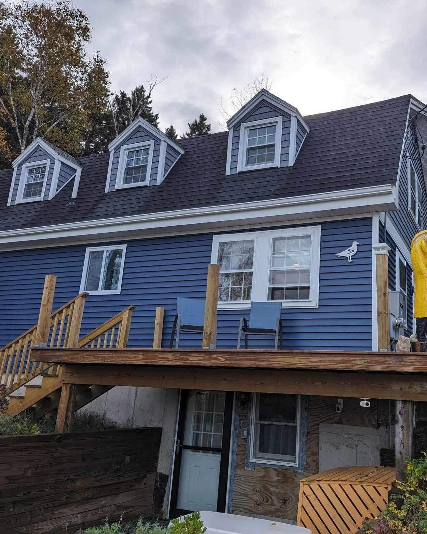 Blue house with dormers, wooden deck, and partially exposed stone basement.