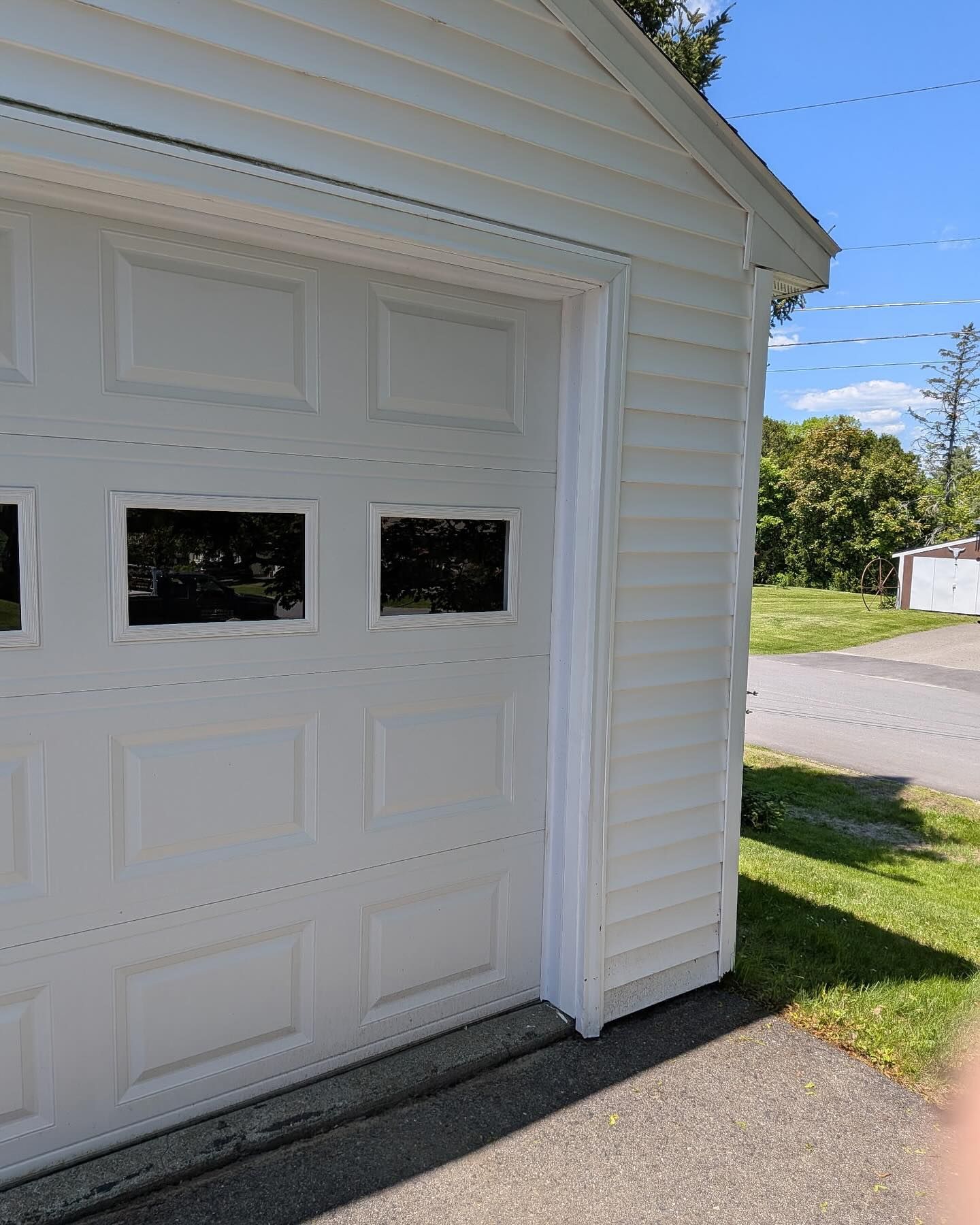 White garage with closed door, windows, and white siding; outside on a sunny day.