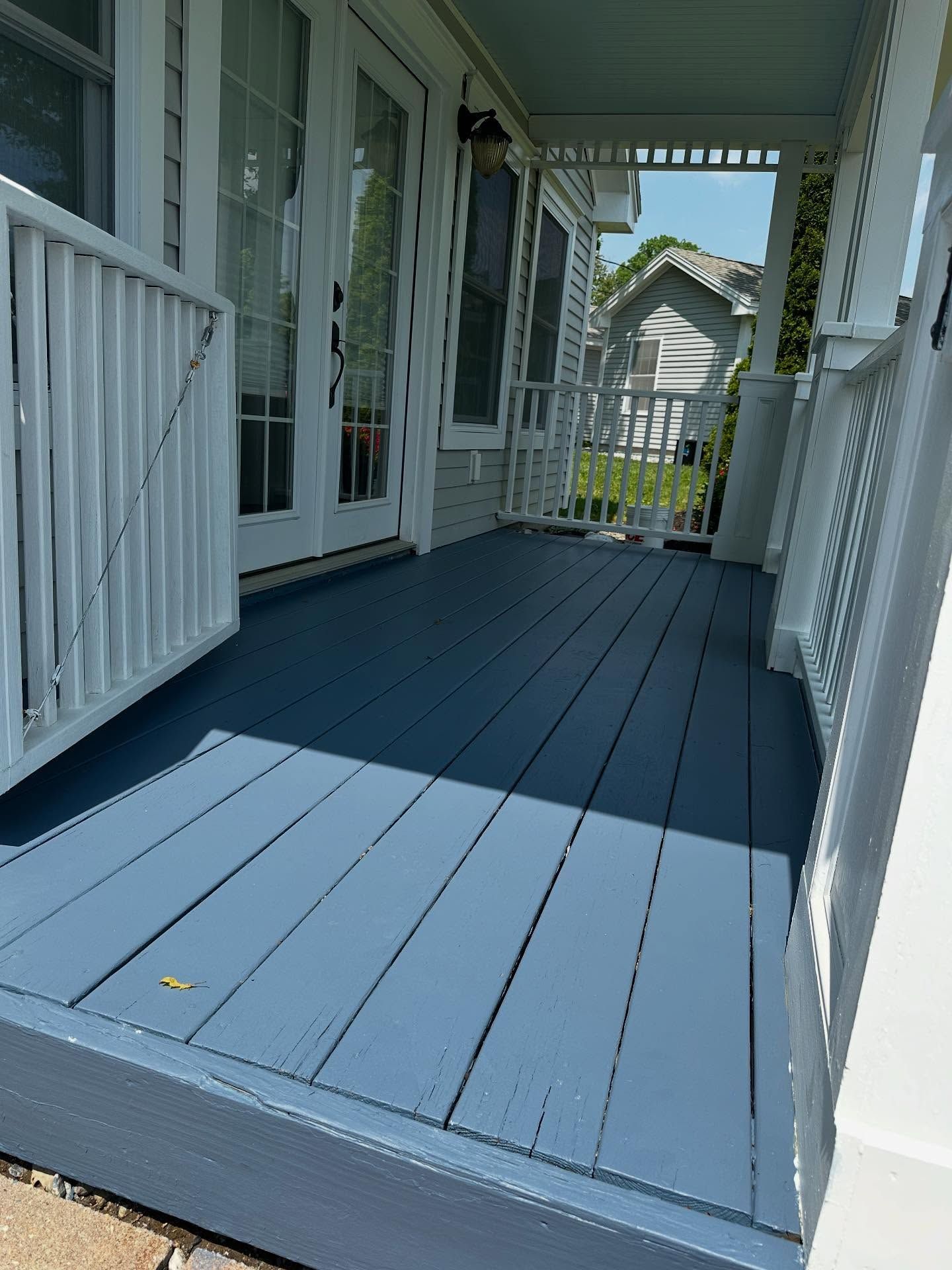 Blue painted wooden porch with white railings and doors; sunny day.