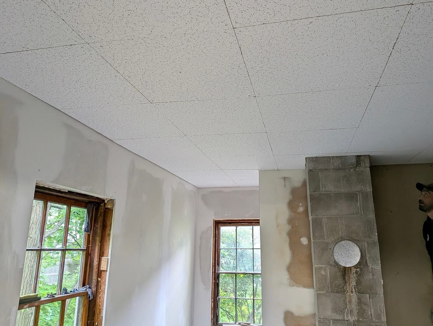 Room interior with textured ceiling, windows, and a brick chimney. Construction in progress.