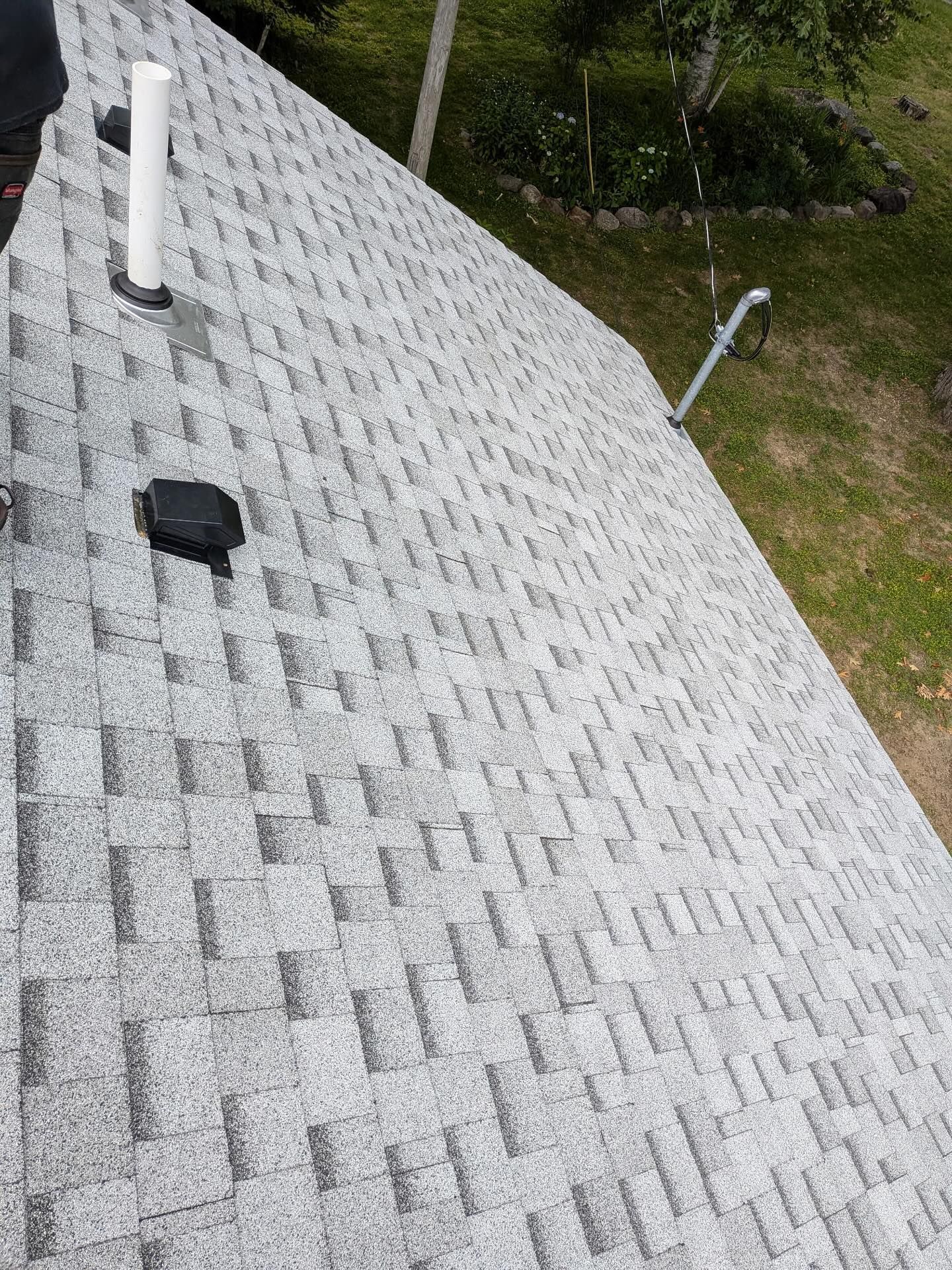 Gray asphalt shingle roof with a white vent pipe and a black object on it.
