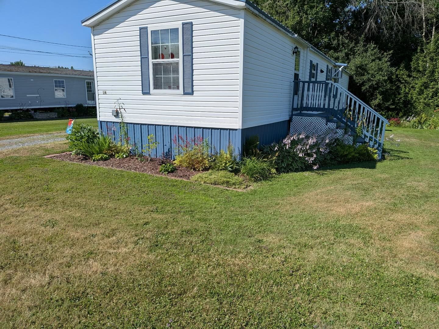 Mobile home with blue accents and landscaping in front yard.