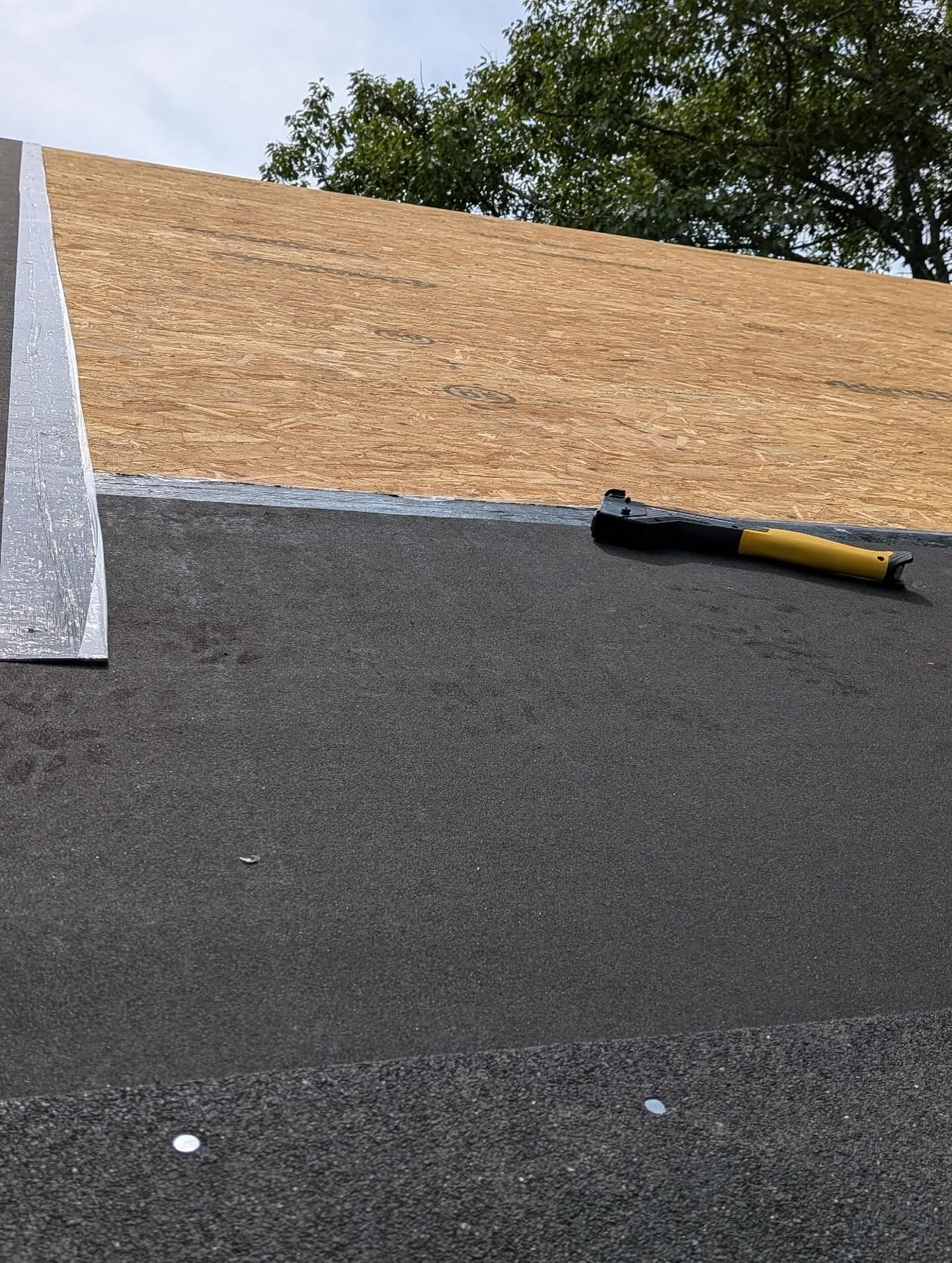 Roof with asphalt shingles and wooden sheathing, a hammer rests on the roof.