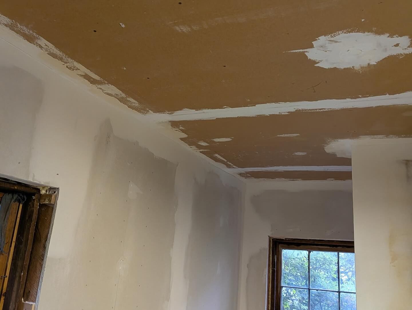 Walls and ceiling under construction; drywall with plaster applied in sections, window visible.