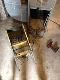 A broken air conditioner is sitting on the floor next to a drill.
