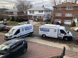 A row of vans are parked on the side of the road in front of a brick house.