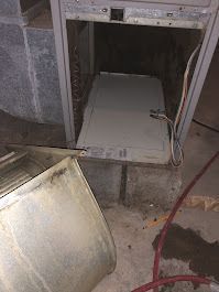 A furnace is sitting in a basement with the door open.