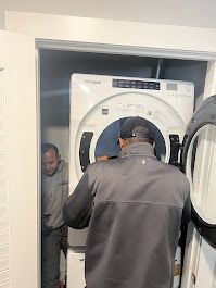 A man is loading a washer and dryer into a closet.