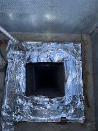 A chimney is covered in aluminum foil and has a hole in it.
