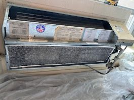 A dirty air conditioner is sitting on the floor in a room.
