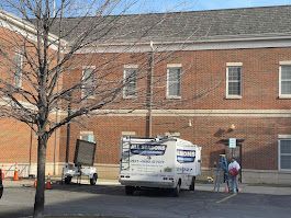 A white van is parked in front of a brick building.