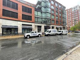 A row of white vans parked in front of a building on a rainy day.