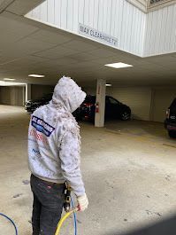 A man in a hoodie is cleaning a parking garage with a hose.