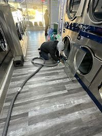 A man is cleaning a washing machine in a laundromat.