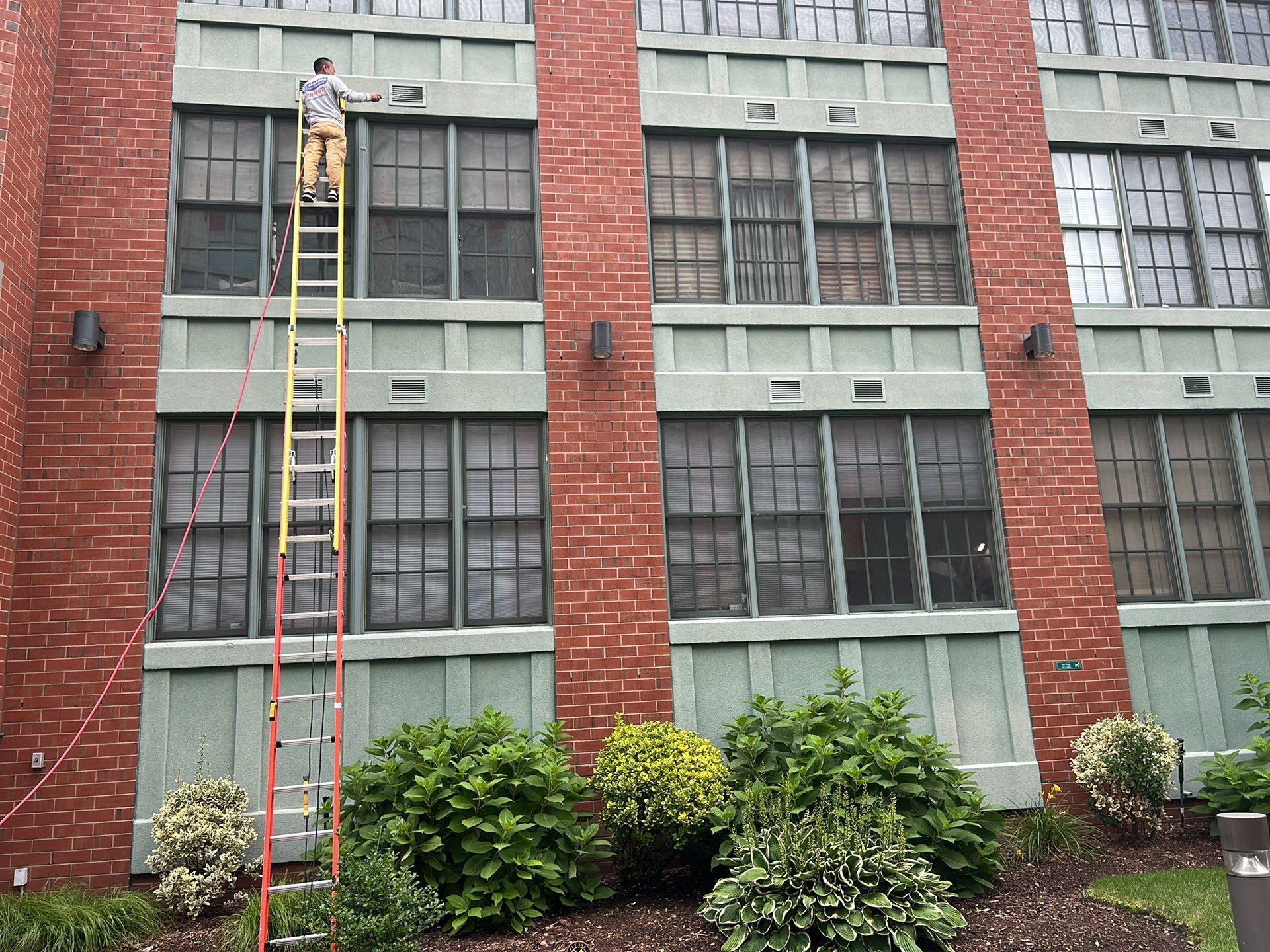 A man on a ladder cleaning the windows of a brick building