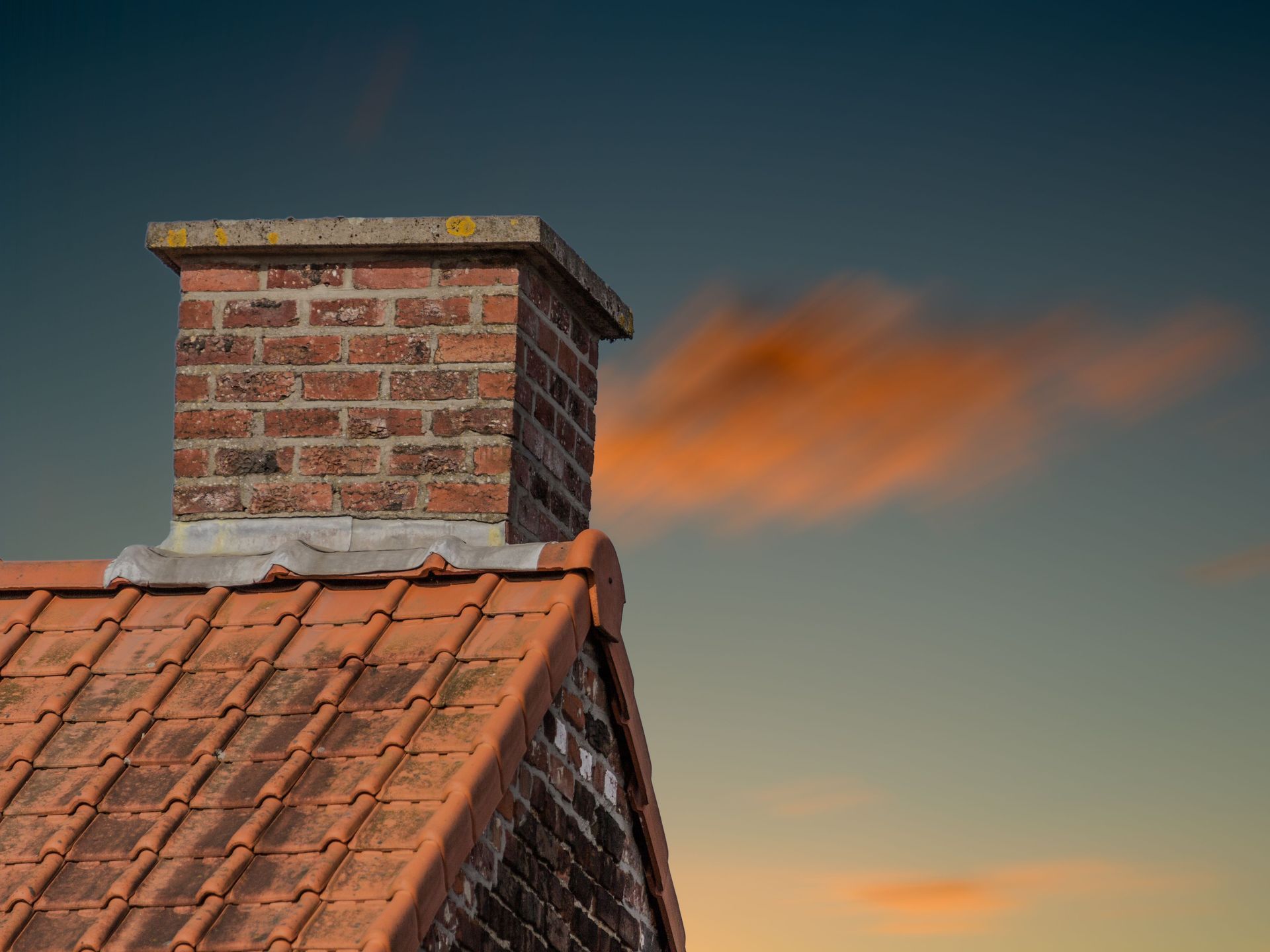 A brick chimney is sitting on top of a tiled roof.