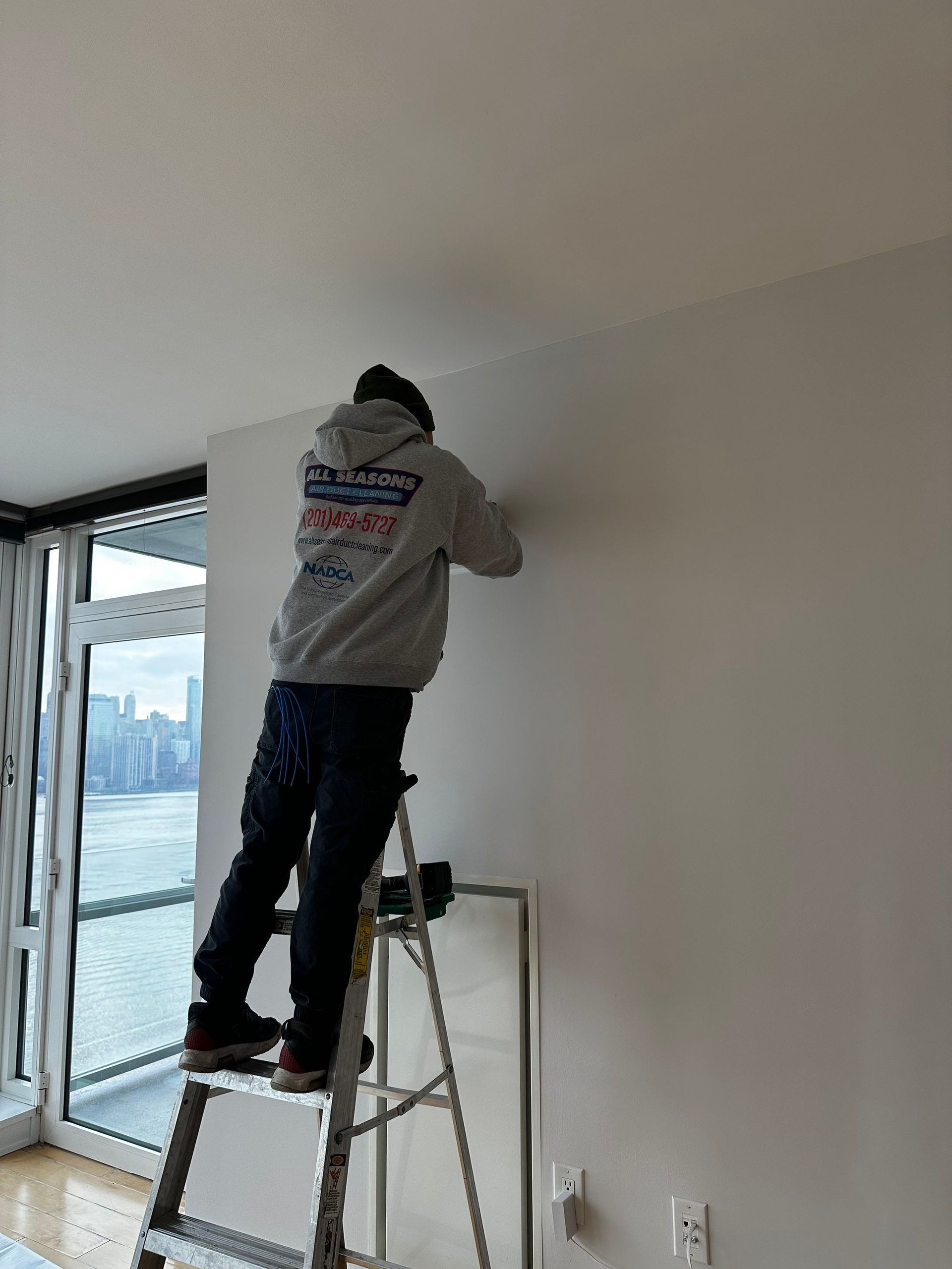 A man is standing on a ladder in a living room.