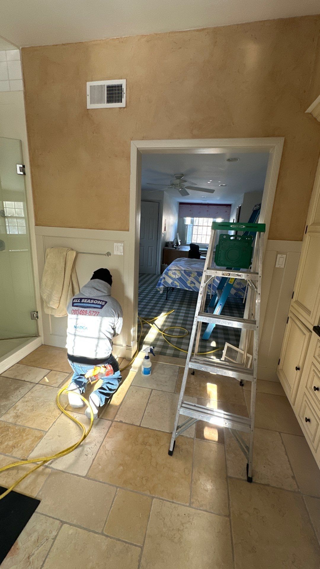 A man is kneeling down in a bathroom next to a ladder.