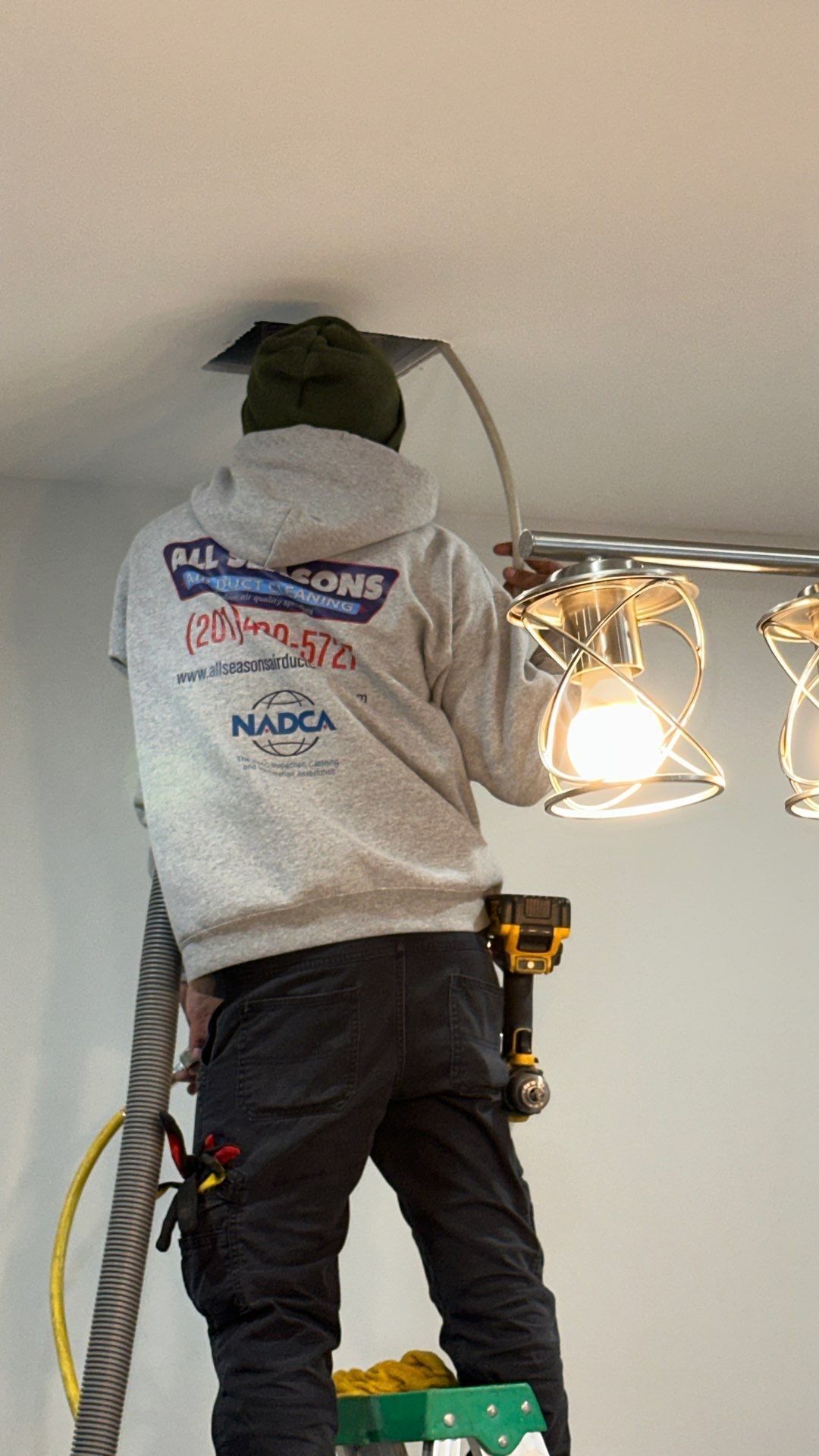 A man is standing on a ladder fixing a light fixture.