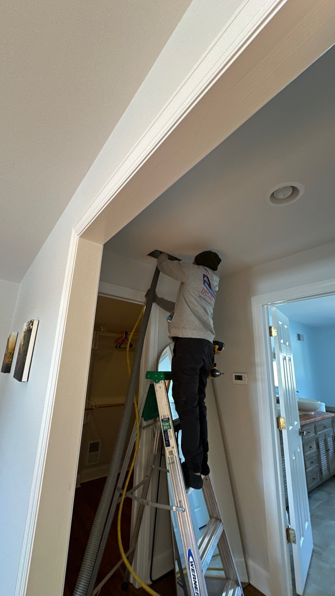 A man is standing on a ladder in a hallway.