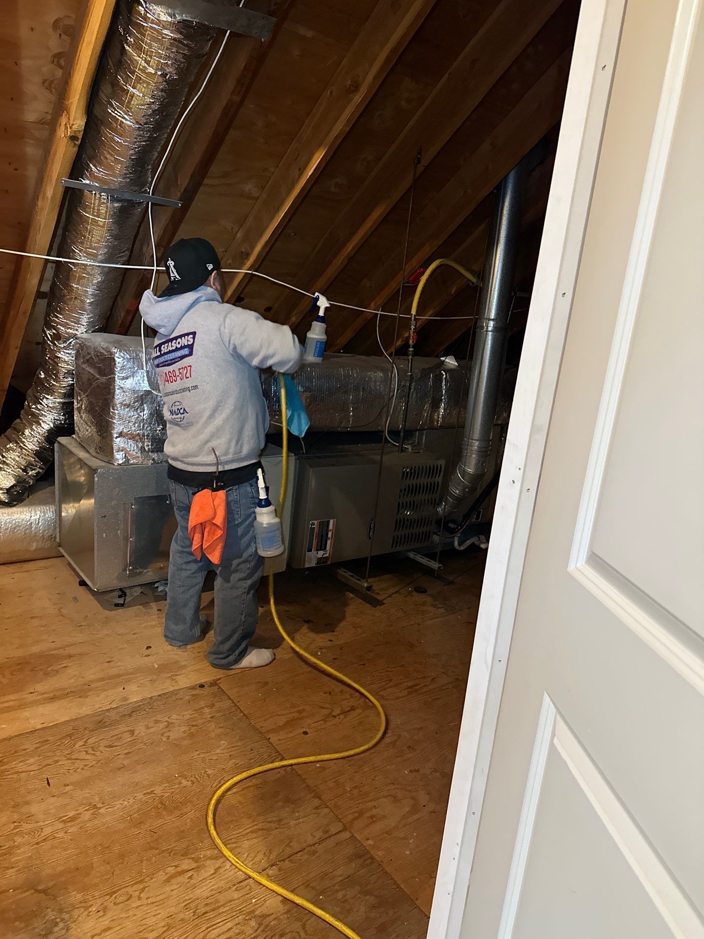 A man is cleaning an air conditioner in an attic.