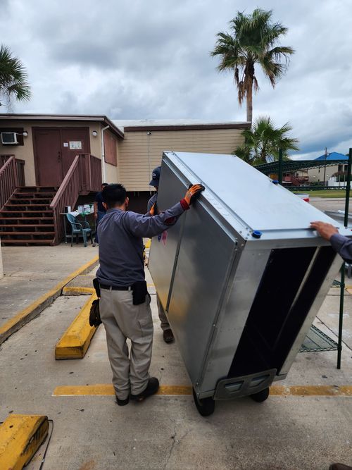 Two men are carrying a large refrigerator in a parking lot