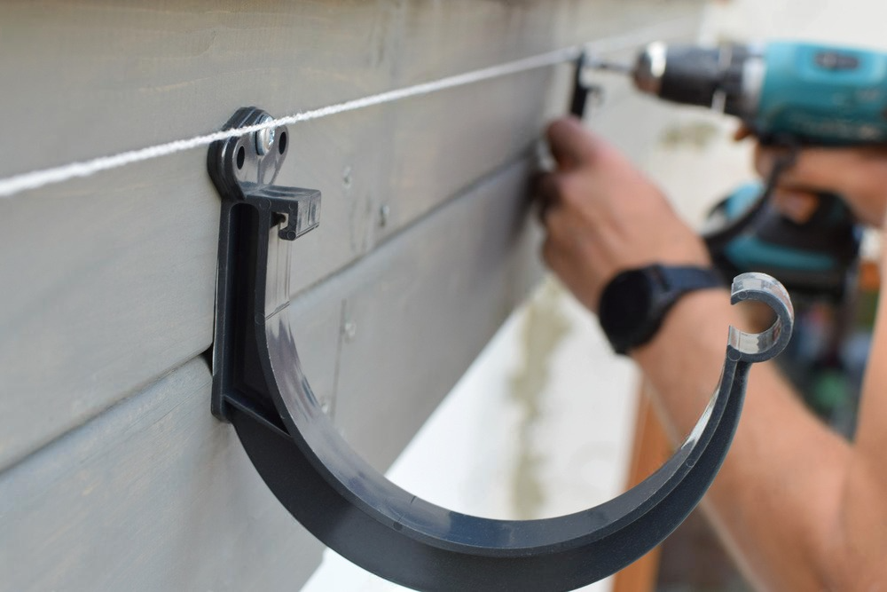 a man is installing a gutter hook with a drill .