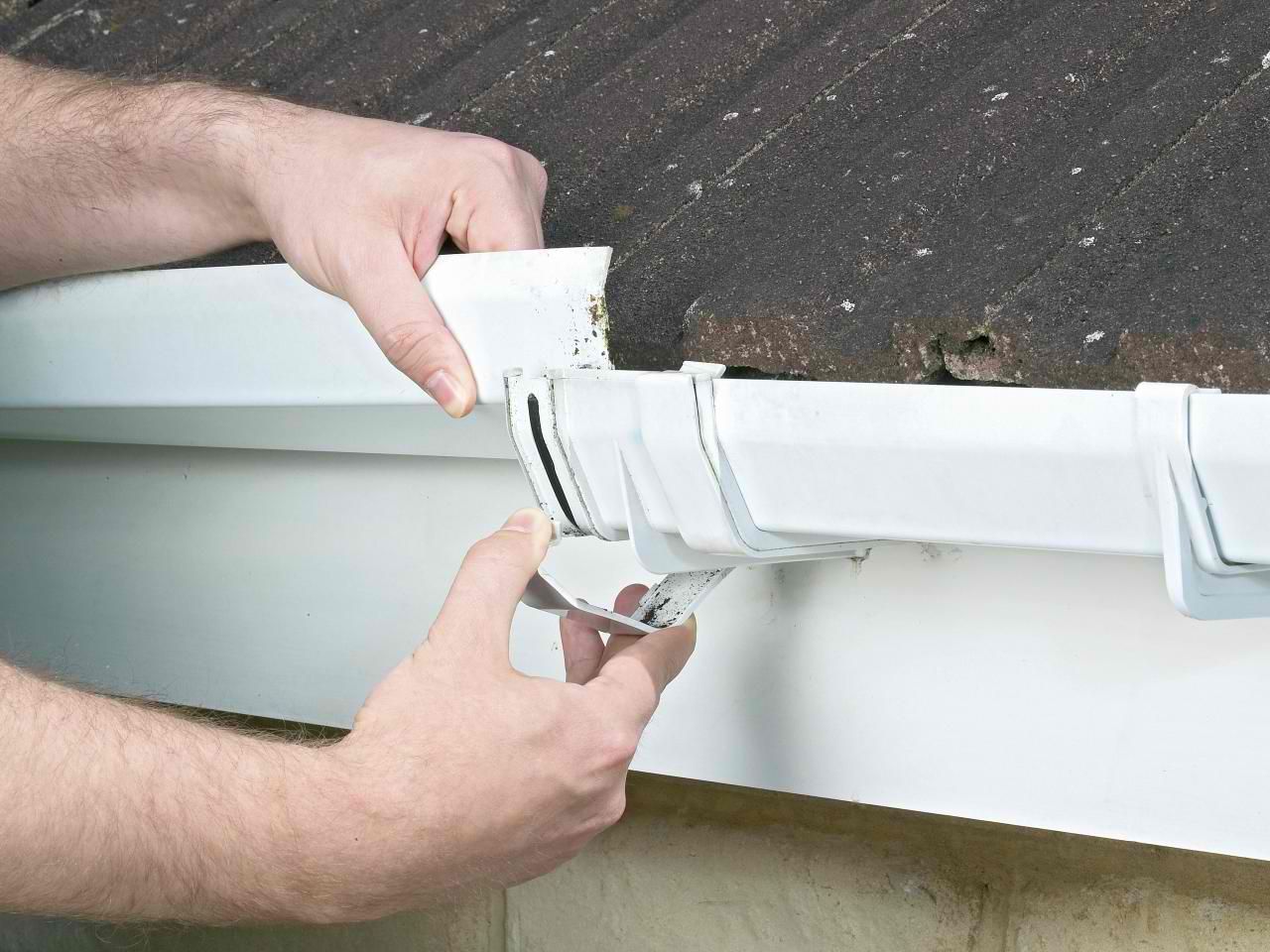 a man is installing a gutter hook with a drill .