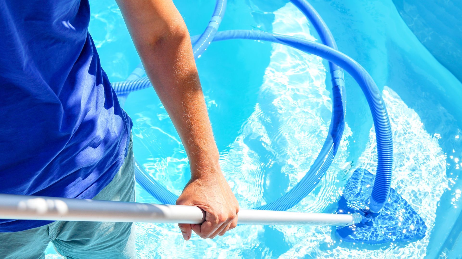 A Person in Blue Shirt Cleaning a Bright Blue Swimming Pool With a Net and Pole — Cascade Pool & Spa Centre in Kempsey, NSW